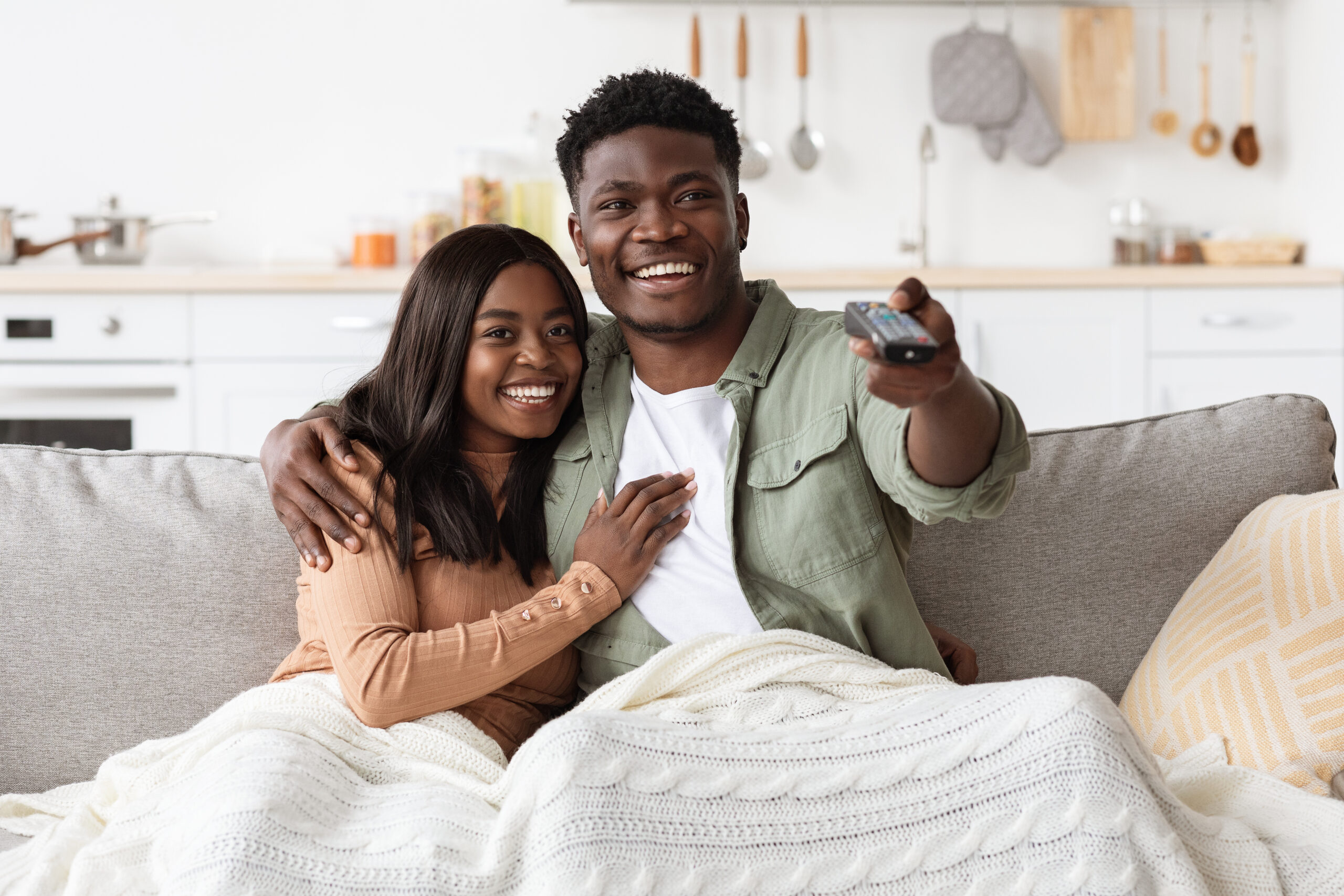 Joyful african american couple watching TV together at home, laughing and bonding, copy space. Happy young black man and woman having fun together on weekend, love and relationships concept