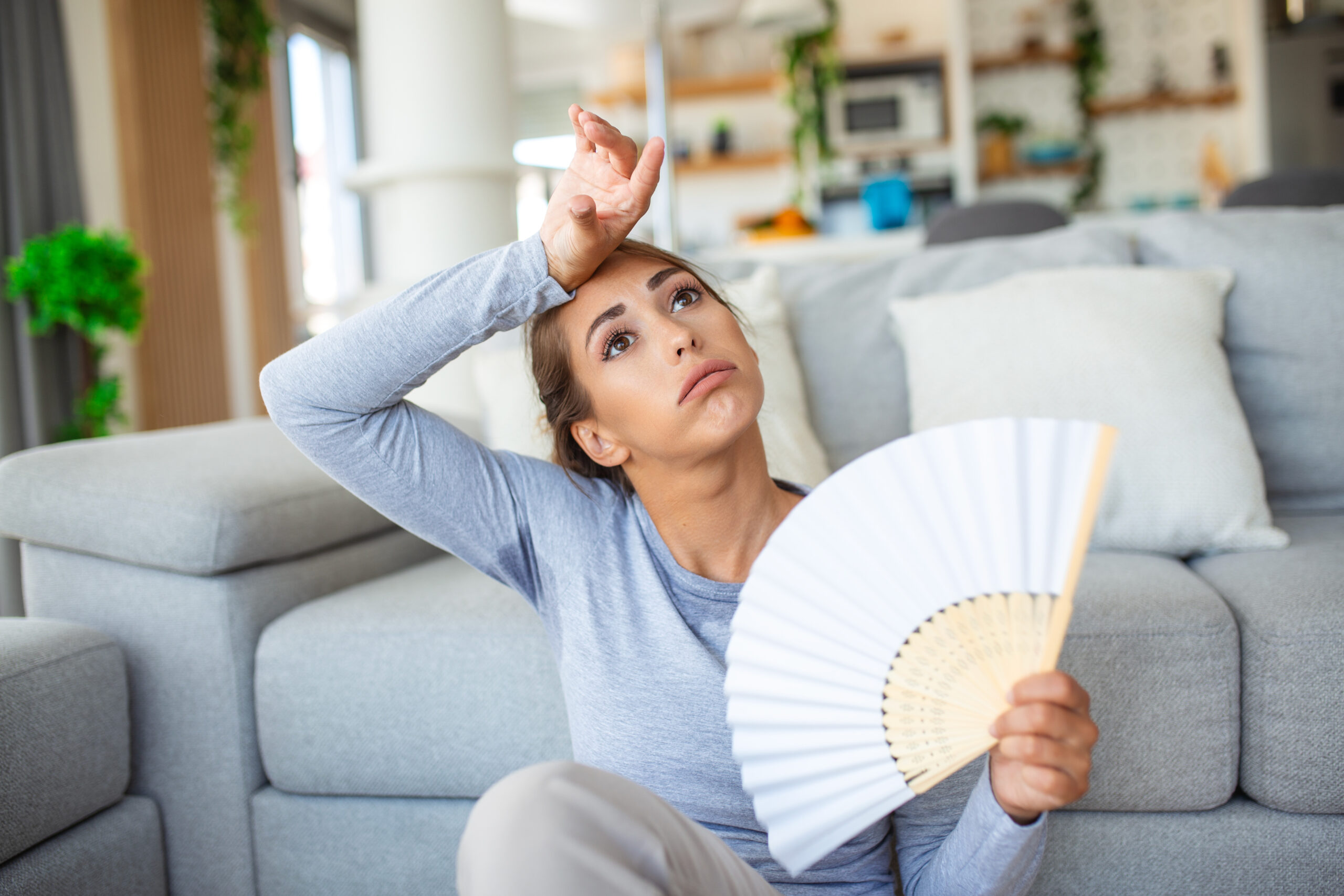 Stressed annoyed woman using waving fan suffer from overheating, summer heat health hormone problem, woman sweat feel uncomfortable hot in summer weather problem without air conditioner